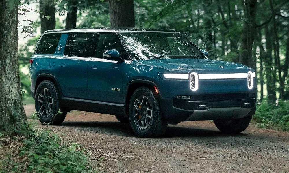 Rivian R1S electric SUV parked beside a forest road.