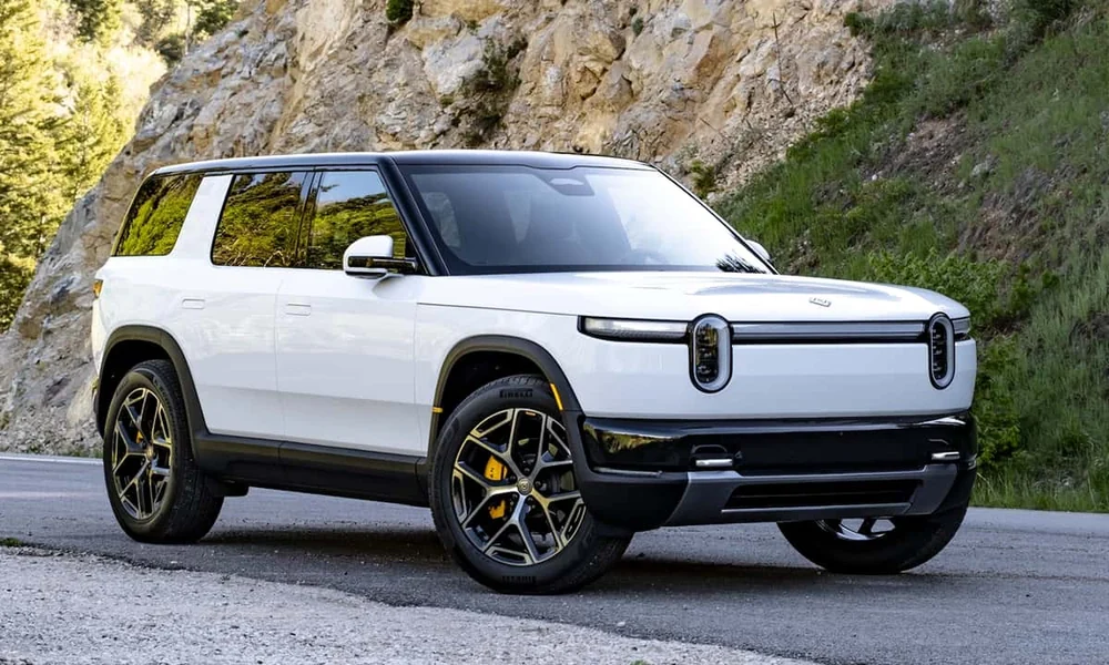 White Rivian R2 electric SUV parked on a road beside a rocky hillside