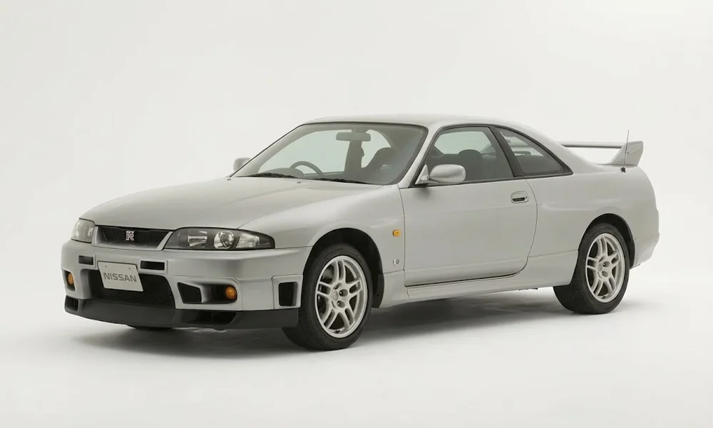 White Nissan Skyline R33 GT-R coupe with alloy wheels, a front air dam, and a large rear spoiler against a white background.