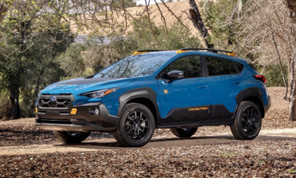 Blue Subaru Crosstrek Wilderness with roof rails parked on a dirt road among trees