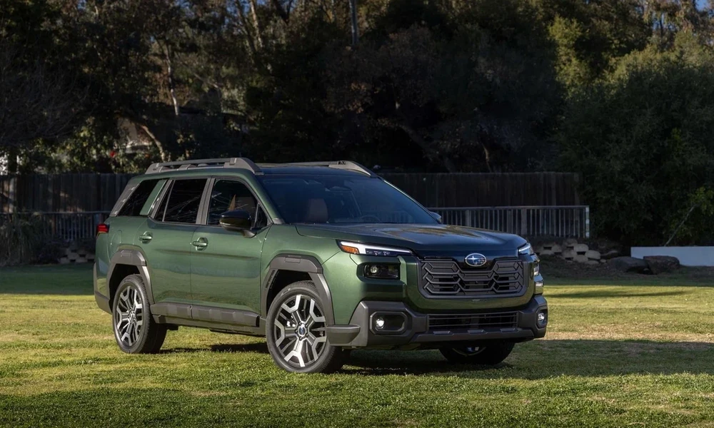 Green Subaru Outback parked on a grass lawn with trees behind it