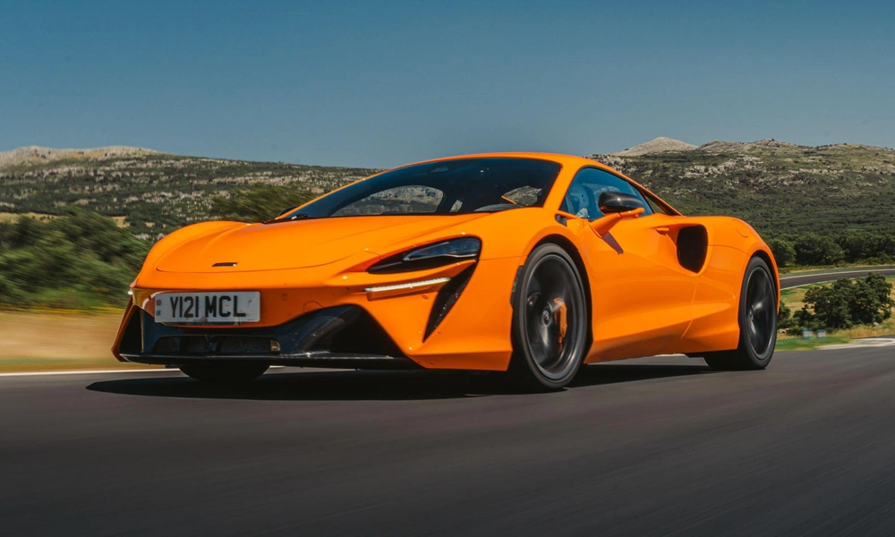 Orange McLaren Artura parked on a scenic road.