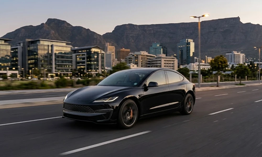 Black Tesla Model 3 driving past office buildings with a flat-topped mountain behind it