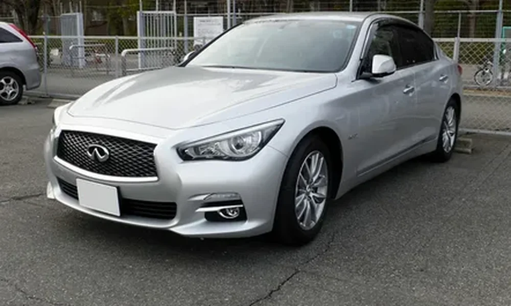 Silver Infiniti Q50 V37 sedan with a black mesh grille, sleek headlights, and alloy wheels, parked on a paved street.