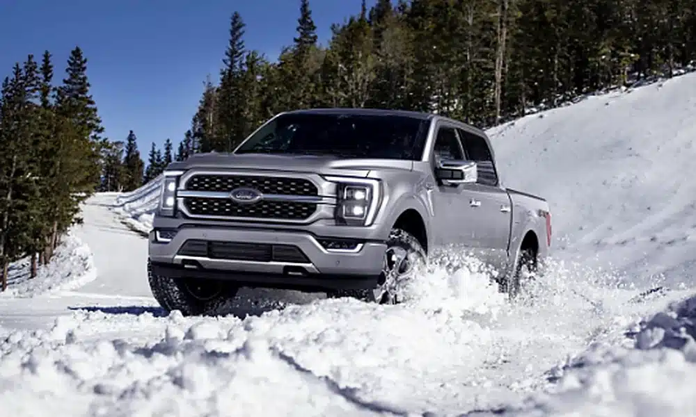 Grey Ford F-150 pickup truck driving through snow on a winter road.