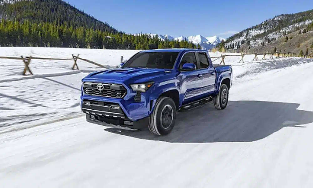 Blue Toyota Tacoma pickup truck travelling on a snow-covered mountain road.